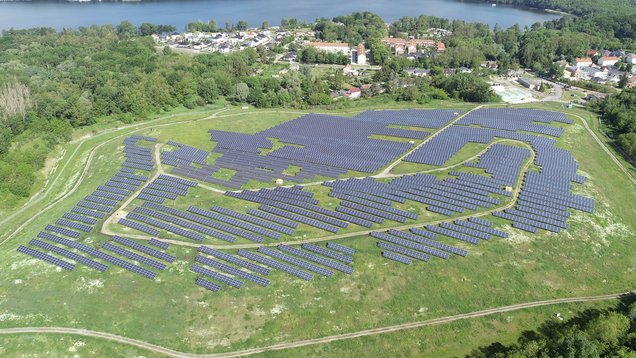 Weite Photovoltaik‑Freiflächenanlage: Zahlreiche dunkelblau‑schwarze Solarpanels reihen sich parallel auf einem offenem Feld.